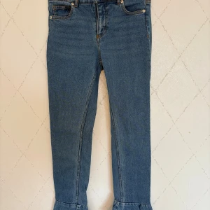 Blå jeans med volang nertill - Säljer ett par blå jeans med volangdetalj längst ner vid bensluten. De är från Monki och är i storlek XS.  Klassisk femficksmodell med normal passform och raka ben. Jeansen är i ett mjukt denimtyg och har en snygg mellanblå tvätt. Perfekta för dig som vill ha något extra på dina jeans.