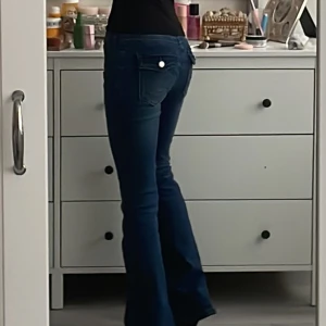 Blå true religion liknande bootcut jeans med fickdetaljer - Säljer ett par blå bootcut jeans som liknar true religion med snygga fickdetaljer bak och dekorativa knappar. Jeansen har klassisk femficksdesign och markerade sömmar.  