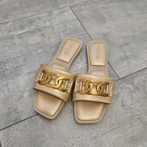 guldiga sandaler med gulddetalj, strl 38 - Snygga guldiga sandaler i storlek 38 med fyrkantig tå och bred rem. aldrig använt, säljer den för att den passar inte mig. jag har en annan variant som finns i min profil också. 