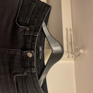 Svarta straight jeans från ZARA - Snygga svarta jeans från ZARA med klassisk femficksdesign och raka ben. Jeansen har silverfärgad knapp och dragkedja framtill, samt tydliga sömmar och bälteshällor. Materialet är jeans med en mörk tvätt som ger en cool vibe.