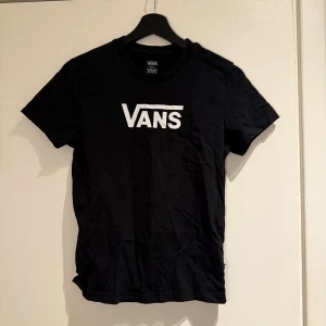 Svart Vans t-shirt med logga - Svart t-shirt från Vans i storlek small med klassisk vit Vans-logga tryckt på bröstet. Modellen har rund hals och korta ärmar, tillverkad i mjuk bomull som är skön mot huden. 