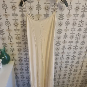 Beige långklänning med smala axelband - Säljer en stilren beige långklänning med smala axelband och rak siluett. Klänningen har minimalistisk design och är perfekt för dig som gillar enkelhet och ljusa färger. Materialet känns mjukt och följsamt mot kroppen.