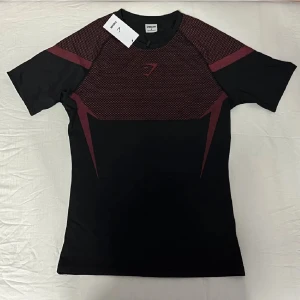 Gymshark onyx - Sportig svart t-shirt från Gymshark med vinröda detaljer och mönstrad ovandel. Tight passform och tillverkad i ett lätt, stretchigt syntetmaterial som andas. Perfekt för dig som vill ha en snygg och funktionell tränings-tisha med cool design. Ett till ett. Denna tröjan är limited edition, alltså går det inte att få tag på liknande t-shirts. Vid någora frågor är det bara att skriva 🤗. 