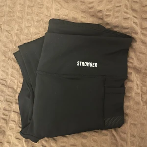 Svarta träningstights från Stronger med fickor (nya) - Signature Pocket Leggings från Stronger med hög midja och praktiska sidfickor, perfekta för mobilen. Endast använda + tvättade en gång, då de är något för små för mig. Snygga detaljer med diskret mönster på fickorna och tight passform som sitter på plats under träning, samt utan framsömmar. Nypris 799 kr.