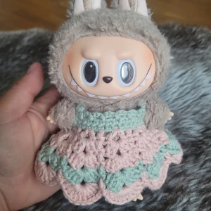 Handvirkad dockklänning i pastell - Supersöt handvirkad dockklänning i ljusrosa och mintgrönt. Klänningen har ett vågigt mönster och är gjord i mjuk bomull. Perfekt för att ge din docka en gullig och unik look. Passar mindre dockor och är lätt att ta av och på.