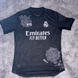 Real Madrid x Y-3 svart fotbollströja - Svart kortärmad Real Madrid fotbollströja från Adidas och Y-3 med vita tryck, ros-motiv och HEAT.RDY-material. Snyggt Real Madrid-emblem på bröstet och coolt Y-3-tryck. Perfekt för dig som gillar limited edition och streetstyle.