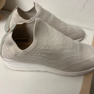 Beige stickade slip-on sneakers  men är som 38 i storlek  - Snygga beige slip-on sneakers från D.A.T.E. med stickad ovandel och vit platt sula. Skorna har en mjuk, vågig struktur i materialet och ljusgrå detalj vid hälen med logotyp. Perfekt för dig som gillar minimalistisk och modern stil.