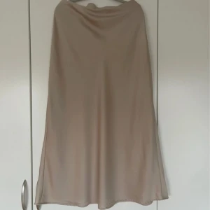 Beige långkjol i satin från Vila - Beige kjol från Vila, strl 42. 100% polyester, använd endast 1 gång - fint skick! Fläckfri, nytvättad och steamad!🤍