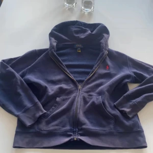 Mörkblå hoodie från Polo Ralph Lauren - Priset är förhandlingsbart! Men lite info om tröjan. Snygg mörkblå hoodie från Polo Ralph Lauren med dragkedja och huva. Tröjan har långa ärmar, två fickor fram och en liten röd logga broderad på bröstet. Perfekt för chill dagar och enkel att matcha med jeans eller joggers.