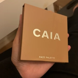 CAIA Face Palette med fyra nyanser - Säljer en CAIA Face Palette Summer edition .med fyra olika puderprodukter: contour i matt brun, bronzer i varm brun, rouge i klar rosa och highlighter i skimrande guld. Paletten är fyrkantig med spegel i locket och har en snygg beige förpackning med metallictext. Väldigt sparsamt använd som man ser på highlightern det står ju frf ”caia”. Nypris 500kr.