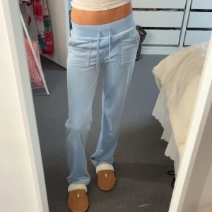 Ljusblå mjukisbyxor Juicy Couture - Säljer ett par ljusblå mjukisbyxor från Juicy Couture med bred resår i midjan och snörning framtill. Byxorna har raka ben, två stora fickor fram, två fickor bak och broderad logga på ena fickan. Supermjukt material som känns skönt mot huden.