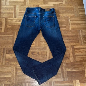 Mörkblå jeans från Nudie Jeans - Snygga mörkblå jeans från Nudie Jeans med klassisk femficksdesign och kontrastsömmar. Jeansen har en rak passform och är tillverkade i slitstarkt denimtyg av bomull. Perfekta för dig som gillar en tidlös och stilren look.