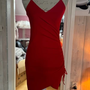 Röd kort klänning från H&M Divided - Snygg röd kort klänning från H&M Divided med smala axelband och v-ringning. Klänningen har en tight passform och cool snörningsdetalj på sidan som ger en rucheffekt. Perfekt för dig som vill sticka ut och känna dig extra fin.