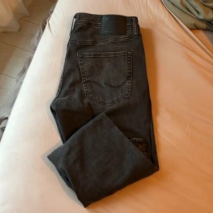 Svarta slim jeans Jack & Jones 32/32 - Svarta jeans från Jack & Jones i modellen Slim/Glenn. Klassisk femficksdesign med snyggt bakficka-detalj och svart läderpatch i midjan. Jeansen har en slim passform och är tillverkade i mjukt denimtyg som sitter skönt hela dagen.