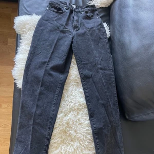 Snygga svarta jeans – rak passform & hög midja! - Stilrena svarta jeans med rak passform och hög midja. Klassisk femficksmodell med bälteshällor och dragkedja. Jeansen har en mörk tvätt och är tillverkade i kraftigt denimtyg som ger en tidlös och elegant look.