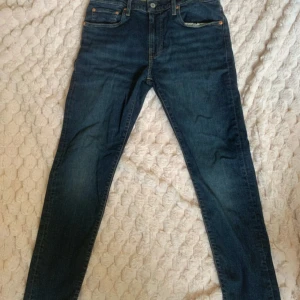 Levi's 512 Slim Taper mörkblå jeans 32x32 - Mörkblå Levi's 512 Slim Taper jeans med stretch, smal passform och avsmalnande ben. Klassisk femficksmodell i jeansmaterial med snygga kontrastsömmar och läderpatch bak. Perfekta för dig som gillar en modern och stilren look.