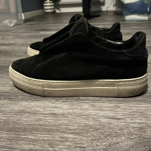 Svarta sneakers från ARIGATO i mocka - Säljer ett par svarta sneakers från Axel Arigato med stilren design och chunky vit sula. Skorna är i mjuk mocka och har en minimalistisk look utan snörning. Perfekta för dig som gillar cleana och moderna vibes. Liten slitning på ena hälen men ingenting stort. Inhandlade för 2299 och har mycket kvar att ge. Storlek 40 men sitter mer som storlek 41. 