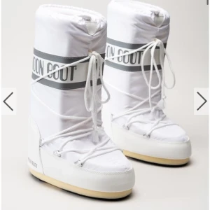 Vita Moon Boots med snörning - Säljer ett par klassiska vita Moon Boots med snörning och bred grå logga runt skaftet. Skorna har en rund tå, platt sula och är tillverkade i syntetmaterial. Perfekta för vintern och riktigt sköna att ha på sig när det är kallt ute.