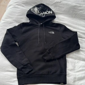 Svart hoodie från The North Face XS - Svart hoodie från The North Face i storlek XS. Klassisk modell med stor logga på huvan och mindre logga på bröstet. Mjuk bomullsblandning, dragsko i huvan och ribbade muddar. Perfekt för chill dagar eller när du vill ha en clean streetstyle.