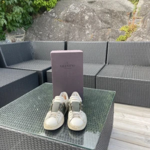 Valentino Garavani sneakers vit/grön - Snygga Valentino Garavani sneakers i vitt skinn med bred grön rem över vristen och klassisk logga på plösen. Skorna har rund tå, snörning och platt sula. Perfekta för dig som vill ha en lyxig och stilren look med streetkänsla. Sulan är nyligen limmad men märks absolut inte och inget man tänker på.🤗🤗