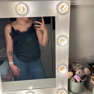 Svart spetslinne från H&M Divided - Svart linnetopp med tunna, reglerbara axelband från H&M Divided. Toppen har v-ringning och dekorativ spets längs urringningen och axelbanden. Tillverkad i mjuk polyesterblandning för skön passform. Perfekt att styla med jeans eller kjol.