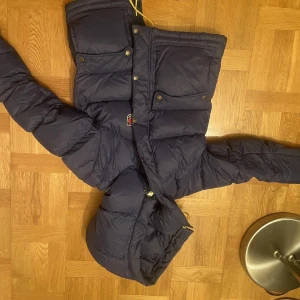 Fjällräven EXPEDITION DOWN LITE JACKET W - Säljer en mörkblå dunjacka från Fjällräven med två stora bröstfickor, dragkedja och tryckknappar. Jackan har huva med gula snören och klassisk Fjällräven-logga på bröstet. Perfekt för kalla dagar och riktigt snygg streetstil.