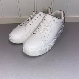 Vita sneakers från Zara - Snygga vita sneakers med stilren design och chunky sula. Ovandel i vitt skinn med detaljer i ljus mocka på hälen. Klassisk snörning och rund tå. Perfekta för dig som gillar en clean look och vill ha bekväma skor till vardags. Använd ca 3 gånger!