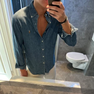 Jeansskjorta från Ralph Lauren - Snygg jeansskjorta från Ralph Lauren i klassisk blå denim. Skjortan har knappar hela vägen, button-down krage och den ikoniska broderade loggan på bröstet. Jag är 188cm och bär storlek S. Hör av er vid frågor;)