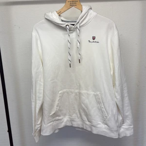 Vit hoodie från Bondelid L - Snygg vit hoodie från Bondelid i storlek XL. Tröjan har huva med snörning, magficka och broderad logga på bröstet. Tillverkad i mjuk bomull, perfekt för chill dagar. Klassisk och enkel design med diskreta detaljer. STORLEK XL MEN SITTER SOM L! 