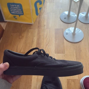 Svarta Vans sneakers med snörning - Klassiska svarta Vans sneakers i canvas med låg profil och platt sula. Skorna har rund tå, svart snörning och diskret Vans-logga på sidan. Perfekta för en clean och stilren look.