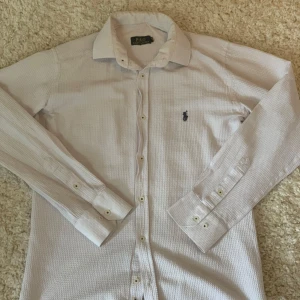 Vit skjorta från Polo Ralph Lauren S - Klassisk vit skjorta från Polo Ralph Lauren i storlek S. Skjortan har lång ärm, knappar framtill och det ikoniska broderade logotypen på bröstet. Tillverkad i bomull med diskret struktur i tyget för en snygg touch.