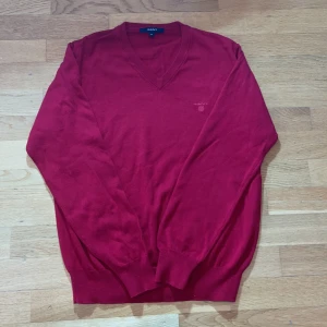 Röd v-ringad tröja från GANT - Röd v-ringad tröja från GANT i 100% bomull. Klassisk modell med ribbade muddar vid ärmslut och nederkant samt diskret broderad logga på bröstet. Perfekt för dig som gillar stilrena och tidlösa plagg.