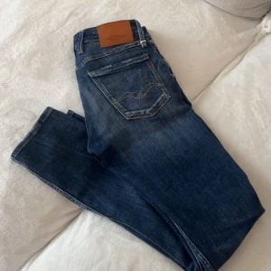 Blå Replay jeans med slitningar - Säljer ett par blå jeans från Replay med snygga slitningar och klassisk femficksdesign. Jeansen har en mellanblå tvätt, läderpatch bak och raka ben. Perfekta för dig som gillar en avslappnad men trendig look. Storlek 29-32 andvända fåtal gånger 