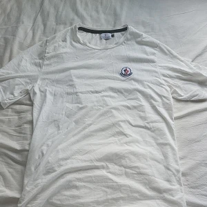 Vit Moncler T-shirt - Moncler t-shirt säljs pga behöver pengar till epa. OBS: tröjan är liten I storleken därför står det att den ör storlek M för den passar perfekt till du med storlek Medium. Tröjan har 2 väldigt väldigt små hål längst ner vid en sömm men syns inte alls.