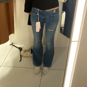 Blå bootcut jeans med slitningar - Snygga blå jeans med bootcut passform och slitningar vid knäna. Jeansen har klassisk femficksdesign, låg midja och är tillverkade i ett stretchigt denimtyg som sitter skönt. Perfekta för dig som gillar en avslappnad men trendig look.