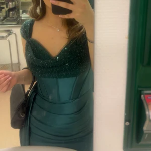 Mörkgrön balklänning med paljetter - Jag säljer min mörkgröna långklänning med glittriga paljetter upptill. Klänningen sitter bra på kroppen och har glansigt material. Perfekt för bal eller fest. Använd endast 1 gång. Köpt för 750kr. Mitt pris 499kr. Går att diskutera priset!🥰 Skriv för fler bilder! 