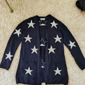 Mörkblå kofta med vita stjärnor H&M - Snygg mörkblå kofta från H&M med vita stjärnor över hela tröjan. Koftan har två fickor framtill och är stickad i mjukt material. Långärmad och loose passform, koftan är i storlek 146/157 och nästintill aldrig använd. Perfekt till den kalla hösten och vintern.