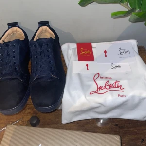 Mörkblå sneakers från Christian Louboutin - Snygga mörkblå sneakers från Christian Louboutin i mocka med klassisk röd sula och broderad logga baktill. Skorna har rund tå, platt sula och snörning. Kommer med originalpåse och certifikat. Perfekta för dig som vill sticka ut med exklusiva detaljer.