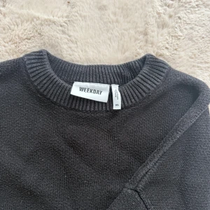 Svart stickad tröja från Weekday - En svart stickad tröja från Weekday i storlek XS. Tröjan har rund halsringning, ribbade muddar och en loose fit som ger en avslappnad vibe. Perfekt att slänga på sig när det är kyligt ute.