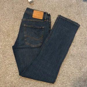Jack & Jones Slim Olenn jeans blå - Snygga blå jeans från Jack & Jones i modellen Slim/Olenn. Jeansen har klassisk femficksdesign, kontrastsömmar och en läderpatch bak i midjan. De är tillverkade i mjukt denimtyg och har en slim passform som sitter snyggt längs benen.