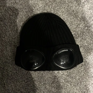 Svart mössa med goggles från C.P. Company - Säljer en stickad cp. Company mössa i one size. Model beanie. Bra skick, kvitto finns. Nypris 1299kr