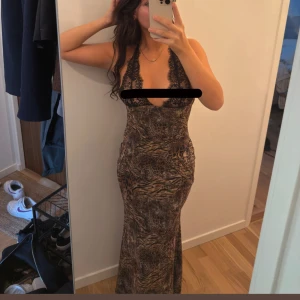 Leopardmönstrad långklänning med spets - Säljer en långklänning med leopard- och zebramönster i bruna och svarta toner. Djup v-ringning med svarta spetsdetaljer och tunna axelband som korsas i ryggen. Klänningen är figurnära och har öppen rygg. SÅÅ SNYGG OCH FIGURSYDD men hittar inte rätt tillfälle så den behöver nytt hem. Köpt utomlands men aldrig använt