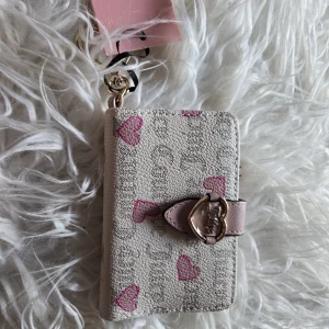 Plånbok Juicy Couture med hjärtan - Supersöt plånbok från Juicy Couture i beige och ljusrosa syntetmaterial med rosa hjärtan och guldfärgad hjärtformad spänne. Flera kortfack, myntfack med dragkedja och plats för ID. Perfekt accessoar för dig som gillar gulliga detaljer.