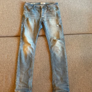 Slim fit jeans från Jack & Jones - Ljusblå slim fit jeans från Jack & Jones, modell Glenn. Jeansen har slitna detaljer och hål på benen för en trendig look. Slim fit, sitter extremt bra, 9/10 i skick, säljer eftersom dom har blivit för små för mig, tveka inte på att höra av er😃