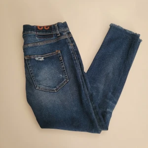 Blå Dondup jeans  - Säljer ett par blå Dondup jeans med snygg slitning på bakfickan och råa, fransiga benslut. Perfekta för dig som gillar en avslappnad och trendig look.