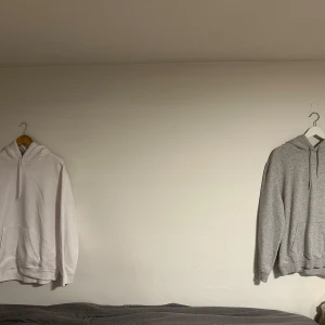 Grå och vit hoodie med huva - Två stilrena hoodies, en i ljusgrått och en i vitt som bara har dammat i garderoben. Båda har klassisk huva med dragsko, magficka och ribbade muddar. Perfekta för chill dagar eller när du vill ha en enkel och snygg look. Materialet känns mjukt och skönt mot huden. Storleken är M men funkar även till L. 🍾💫