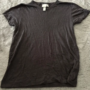 Mörkgrå t-shirt i linne från H&M - En basic mörkgrå t-shirt från H&M i mjukt och svalt linne. Klassisk rund halsringning och korta ärmar. Perfekt för en chill och enkel stil, lätt att matcha med allt.