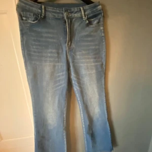 Ljusblå bootcut jeans med rå kant - Säljer ett par ljusblå jeans med bootcut ben och råa, avklippta benslut. Jeansen har klassisk femficksdesign och snygga slitningar framtill för en cool, avslappnad look. Perfekta till sneakers eller boots.