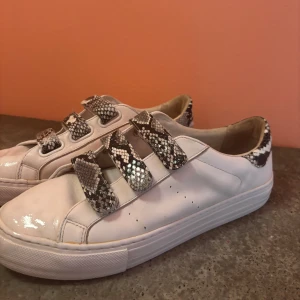 No Name vita sneakers med snake-detaljer - Snygga vita sneakers från No Name med coola ormskinnsmönstrade kardborreband och detaljer på hälen. 