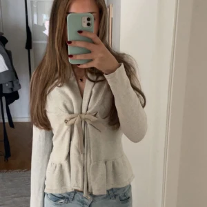 Beige kofta med rosett från Odd Molly - Supersöt beige kofta från Odd Molly med volangkant nertill och knytband i midjan som bildar en rosett. Jättemysig och perfekt till hösten. Väldigt bra skick💕💕